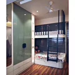 This kids' room is designed for both play and rest. It features a custom-built bunk bed with an integrated ladder and a full-wall wardrobe with sleek glass shutters and open display niches.