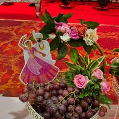 A simple yet elegant fruit platter. This silver bowl is filled with fresh grapes and decorated with a floral arrangement and a cutout of a traditional dancing couple, perfect for a sangeet or reception.