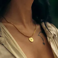 A gold round pendant engraved with the Cancer zodiac sign. Worn on a herringbone chain, this piece is a stylish way to celebrate one's astrological sign.