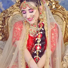 A joyful moment captured. This bride is wearing a stunning red and gold lehenga with matching kundan jewellery. Her makeup features bright pink eyeshadow and a radiant smile.