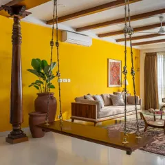 In our 'Vasudhalayah' project, we created a warm, ethnic living room centered around a traditional wooden swing and antique Chettinad pillars. The vibrant yellow accent wall and custom teak furniture create an inviting space for family gatherings.