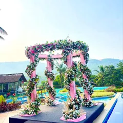 A vibrant pink floral mandap set against a stunning poolside and mountain view. The structure is wrapped in pink fabric and adorned with spiraling garlands of flowers, creating a cheerful and picturesque setting for a destination wedding.