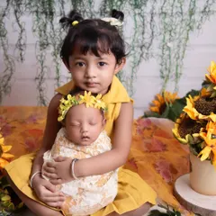 Dressed in matching yellow, this big sister holds her new baby sibling in a sunflower-themed shoot. Coordinating outfits can make family photos even more special.