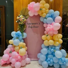 An elegant and modern baby shower backdrop. This setup uses a beautiful pastel color palette of pink, blue, and yellow balloons, accented with dried palm leaves and fresh flowers for a sophisticated look.