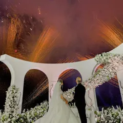 A crescendo of fireworks illuminates the night sky as the couple shares their first moment as husband and wife. The grand architectural mandap, adorned with white florals, provides a spectacular backdrop for this unforgettable memory.