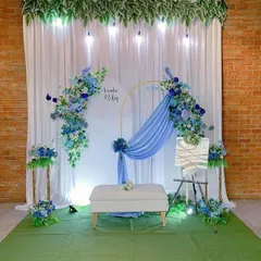 A modern engagement backdrop with a cool blue and white color palette. The setup includes a white arched panel, an asymmetrical blue floral arrangement on a gold frame, and a comfortable white bench for the couple.