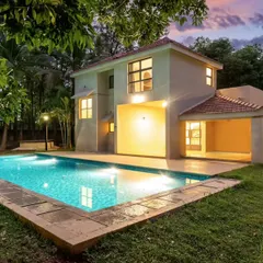 A beautiful villa with a private pool, photographed at twilight. The warm lights from the house and the cool blue of the pool create a stunning contrast against the colorful sunset sky.
