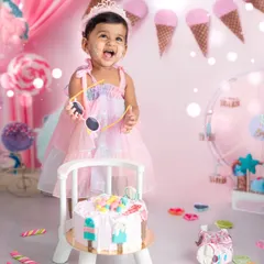 A candid moment of delight during a first birthday cake smash. Dressed in a pastel gown amidst a sweet-themed backdrop, this little one enjoys her special treat, creating a perfect memory.