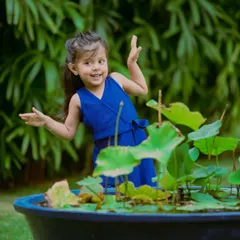 With a playful expression and hands up, this little girl is having a wonderful time during her outdoor photoshoot. The natural greenery provides a beautiful, vibrant background.