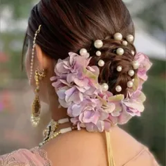 An elegant bridal bun, intricately woven and adorned with fresh lavender flowers and pearls. This kind of detailed hairstyling is perfect for a sophisticated wedding or reception look.