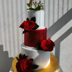 A striking three-tier wedding cake. The combination of clean white tiers, a sparkling red glitter tier, and fresh red roses creates a bold and romantic statement.
