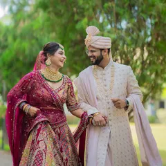A candid, joyful moment of a couple walking hand-in-hand during their Gujarati wedding celebrations, showcasing their vibrant red and cream outfits.