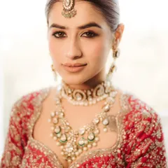 A classic bridal beauty shot. This close-up on Varsha highlights her flawless makeup and stunning Polki and emerald jewelry, capturing the elegance of her bridal look.