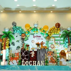 A 'Wild One' first birthday party for Lochan. This grand setup features a leafy backdrop, animal print pedestals, palm tree cutouts, and a full cast of jungle friends, creating an exciting atmosphere for a milestone celebration.