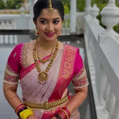 A full view of a stunning bride ready for her ceremony. The vibrant pink and cream saree is paired with classic gold jewelry and a makeup look featuring a bold pink lip and defined eyes, creating a cohesive and regal appearance.