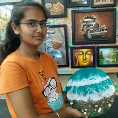 A student holding her beautiful resin art piece depicting a beach scene. Learn to create realistic waves and textures using resin, sand, and shells in our specialized workshops.