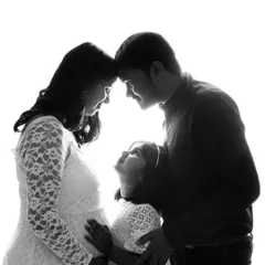 A beautiful black and white silhouette capturing an intimate family moment. A mother, father, and their young daughter come together, their profiles highlighted against a bright white background, focusing on the connection and anticipation for the new arrival.