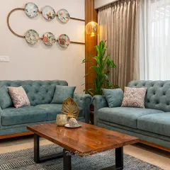 We designed this living area to reflect a modern Indian contemporary aesthetic, perfect for a young couple. The space features elegant teal tufted sofas, a solid wood coffee table, and unique ceramic plate wall decor, creating a warm and stylish environment that feels both timeless and fresh.