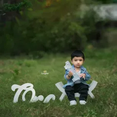 A charming outdoor portrait for a toddler's milestone shoot. This little boy is celebrating turning one, sitting proudly with a 'One' prop in a beautiful, natural park setting.