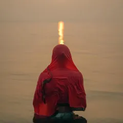 A woman takes a holy dip in the Ganges at sunrise, her red saree a stark contrast against the calm, golden water. This is a moment of pure faith, a quiet prayer in the heart of Varanasi's spiritual landscape.