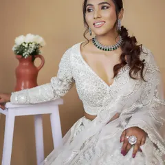A model seated gracefully in the white embroidered lehenga, paired with a contrasting green necklace for a pop of color.