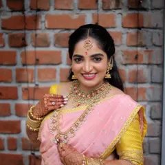 A stunning bridal portrait against a simple brick wall. The contrast makes her beautiful pink and yellow saree and intricate jewelry pop.