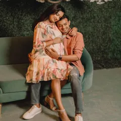 A sweet and tender portrait of an expecting couple on a green sofa. The focus is on their happy expressions and the gentle way they hold the baby bump.