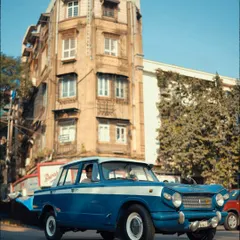 A vintage blue car driving down a street in South Mumbai. This shot evokes a sense of nostalgia and timelessness, a piece of the city's past still moving through its present.