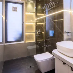 A modern bathroom featuring a glass-enclosed shower with built-in, backlit shelving for toiletries. The combination of dark floor tiles and lighter wall tiles creates a balanced and sophisticated look.