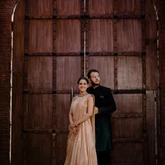 Dheeraj and Navdeep pose in front of a massive, rustic wooden door, giving their pre-wedding portrait a grand and historic feel. Her golden gown and his dark sherwani add to the regal look.