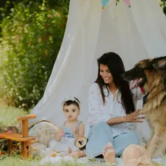 A candid moment of the mother petting their family dog while the baby plays nearby. It's a beautiful, relaxed scene of a happy family day.