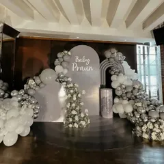 An elegant and sophisticated baby shower for "Baby Praun" in a silver and grey monochrome palette. The setup features a full stage with arched backdrops and beautiful cascades of balloons and white flowers.