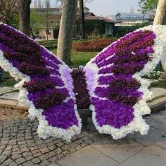 The flower butterfly sculpture seen from the front, showcasing the intricate color pattern of purple, white, and deep violet flowers.