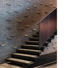 A staircase at the BCG office is framed by a textured brick wall where bricks protrude at intervals. This detail adds a layer of craftsmanship and tactile interest to a functional element.