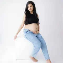 A confident and modern portrait. The mom-to-be rocks a casual look with a black crop top and jeans, showcasing her baby bump with style.