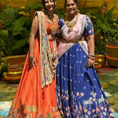 A beautiful portrait of sisters, one wearing my orange silk lehenga with a hand-painted border and the other in a custom blue printed lehenga. It shows how I can create distinct yet complementary outfits for your bridal party.