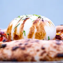 A side-profile of the burrata on the pizza, highlighting its height and the beautiful char marks from the grill. It builds anticipation for the cut.