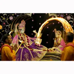 An 'aarti' ceremony in progress, with a priest waving a flaming lamp before the temple deities. The photograph captures the dramatic arc of the fire and the deep reverence of the moment.