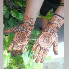 This is an example of modern cut-work, or negative space, mehndi. The design creates a beautiful contrast on the skin, featuring a central floral medallion surrounded by delicate swirls, with a matching vine pattern on the wrist.