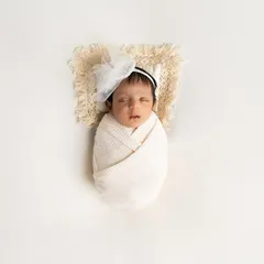 A classic, minimalist portrait. The baby is swaddled in a simple cream wrap against a clean white background, creating a timeless and pure image.