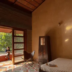 The bedroom is a serene space with exposed earth walls and a large doorway that opens to the outdoors, blurring the boundary between inside and out.