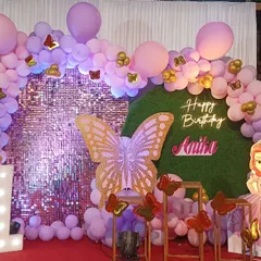 A beautiful butterfly theme with a purple shimmer wall and a grass backdrop. The decor includes a large butterfly prop, a Sofia the First cutout, and a purple balloon arch.