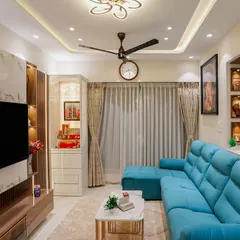 A vibrant living room designed for comfort. The plush turquoise sofa becomes the centerpiece, complemented by a marble-finish TV wall, gold accents, and unique ceiling lights that add a touch of glamour.