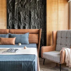 For the Rustic Reverie apartment, I designed this master bedroom to be a sanctuary of texture. A custom-chiseled stone panel serves as a dramatic backdrop, balanced by the warmth of wood paneling and a rich leather bed frame, creating a space that is both bold and serene.