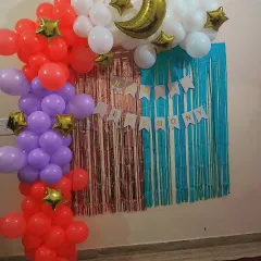 A simple and sweet backdrop for a baby's naming ceremony. The decoration includes a colorful balloon arrangement with a moon and stars theme against a tinsel curtain.