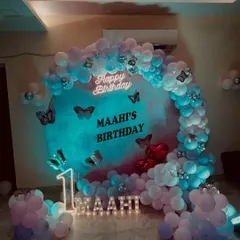 A beautiful butterfly themed first birthday party. The circular backdrop is surrounded by a pastel balloon arch, with a neon 'Happy Birthday' sign, marquee number '1', and light up letters for the name 'Maahi'.