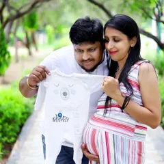 An expecting couple shares a quiet moment in a park, looking at a baby onesie together. This image from an outdoor maternity photoshoot in Noida captures the sweet anticipation of welcoming a new family member.