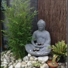 A meditative space created with a sitting Buddha statue, young bamboo plants, and a bed of smooth white river stones. The natural textures create a simple yet elegant design.