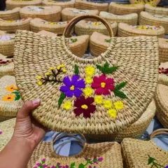 A hand holds up one of our beautifully embroidered bags, with many more in the background. This demonstrates the product in hand and also our capacity for bulk production, perfect for wholesale inquiries.