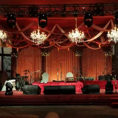 The stage for a Sufi night, draped in red with strings of marigolds and illuminated by grand crystal chandeliers, creating a soulful and poetic atmosphere.